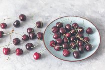 Fresh cherries in ceramic bowl and on ceramic surface — Stock Photo