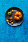 Vari tipi di pomodori su un piatto su uno sfondo blu — Foto stock