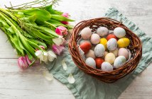 Un nido de Pascua lleno de coloridos huevos de Pascua y un montón de tulipanes - foto de stock