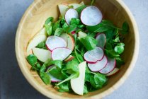 Салат из ягнят с яблоками и редькой в деревянной миске — стоковое фото