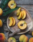 Деревянная тарелка из обрезанных персиков с листьями и ножом — стоковое фото