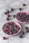 Свежие вишни на розовых тарелках на бетонной поверхности — стоковое фото