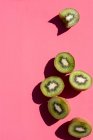 Kiwi-Hälften, eine mit herausgebissenem Biss, auf rosa Oberfläche — Stockfoto