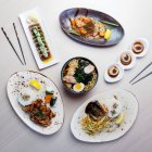 Современные японские блюда на столе: куриный рамен, тунец татаки, цыпленок соба, соус чили эби, лосось гриль и гребешки с мисо-соусом — стоковое фото