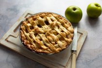 Apple pie in tin with knife on wooden board — Stock Photo