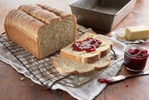 Fresh baked bread loaf, sliced and topped with butter and berry jam — Stock Photo