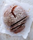 Round spelt wholegrain bread on paper, sliced — Stock Photo