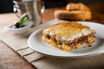 Piece of greek mousaka served on a plate and bread on the background — Stock Photo