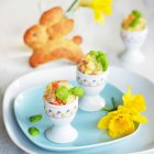 Potato salad with carrot, apple, peas and mayonnaise served in egg cups, with a yeast bread Easter bunny and daffodils in the background — Stock Photo