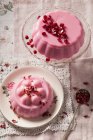 Two pastel pink milk jellies on vintage glass cake stand and plate one covered with pomegrante seeds the other with dried rose petals shot overhead on vintage lace napkin — Stock Photo
