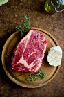 Un steak cru à l'ail et au romarin sur une planche de bois — Photo de stock