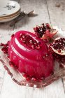 Geléia rosa brilhante coberta de sementes de pomegrante em um prato de vidro vintage com um pomegrante dividido no fundo — Fotografia de Stock