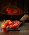 Um tomate cortado pela metade com gotas de água em uma faca velha dos açougueiros — Fotografia de Stock