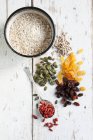 Raisins, golden raisins, pumpkin seeds, sunflower seeds and goji berries in small piles, and a bowl of oats — Stock Photo