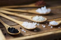 Verschiedene Arten von Lebensmitteln grobes Salz in Holzlöffeln auf dunklem Hintergrund — Stockfoto