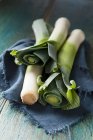 Three whole leeks on a blue cloth and green wooden surface — Stock Photo