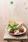 Ensalada vegana (trigo einkorn, tomates, lechuga de cordero, anillos de cebolla roja, lechuga iceberg, berro, pimienta negra) en un bol de hojas de palma - foto de stock
