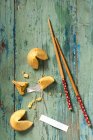 Three fortune cookies one broken open with fortune paper coming out and blank fortune paper for your message on a aqua green blue board and chopsticks - foto de stock
