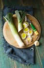 Overhead shot of two leeks on a round wooden chopping board being sliced by a retro wooden handled knife and navy cloth and green wooden background — Stock Photo