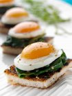 Peppered quails eggs in spinach on an English muffin canapes — Stock Photo