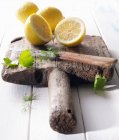 Halved lemons on an old wooden board with parsley, dill and a knife — Stock Photo