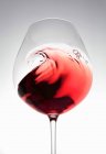 Vin rouge créant une vague dans un verre — Photo de stock