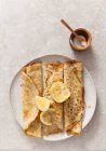 Three rolled pancakes pn a off white texture plate with lemon wedges on a stone surface propped with wooden sugar bowl and spoon — Stock Photo