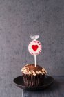 Una magdalena con glaseado de chocolate y avena con un lolly en forma de corazón pegado en la parte superior - foto de stock