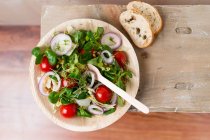 Vegan salad (einkorn wheat, tomatoes, lamb's lettuce, red onion rings, iceberg lettuce, cress, pepper) in a palm leaf bowl — Stock Photo
