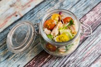 A pasta salad in a glass jar with tomatoes, chicken strips and pecorino — Stock Photo