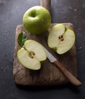 Granny Smith apples, whole and halved, on an old wooden board with a knife — Stock Photo