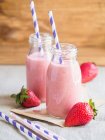 Strawberry smoothies in glass bottles with drinking straws — Stock Photo
