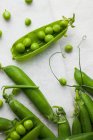 Fresh shelled peas on pale marble and linen background — Stock Photo