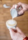 Um barista derramando leite espumado em uma xícara de cappuccino — Fotografia de Stock