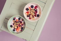 Yoghurt with granola, blackberries, rose petals and cherries in bowls — Stock Photo