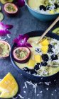 Cuenco de batido de mango rematado con fruta de la pasión, una orquídea, mora, kiwi amarillo y coco - foto de stock