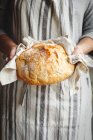 Woman wearing an apron holds freshly baked artisan bread in her hands — Stock Photo