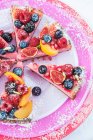 Blick auf Erdbeer-Käsekuchenscheiben auf drei rosa und roten Tellern mit frischem Obst und Himbeercoulis — Stockfoto
