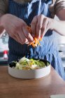 A man scattering julienne carrots over a vegetable salad — Stock Photo