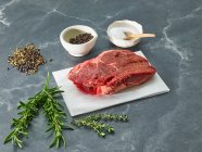 Raw sirloin steak on a piece of paper surrounded by herbs and spices — Stock Photo