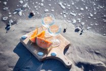 Two glasses of white wine and cantaloupe melon on sand beach — Stock Photo