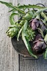Alcachofras verdes e roxas em uma tigela de metal — Fotografia de Stock