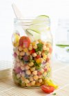 A chickpea salad in a glass jar with tomatoes, peppers, red onions, spring onions, spices, limes, olive oil and fresh parsley — Stock Photo