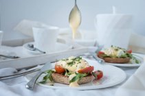Eggs benedict with hollandaise sauce, rocket, and tomatoes on toast - foto de stock