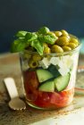 Una ensalada de tomates, pepinos, feta, aceitunas verdes y albahaca en un vaso - foto de stock