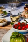 Outdoor table with tomatoes, pasta with cheese and pepper, shrimp skewers, artichokes and white wine — Stock Photo