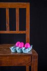 Uova di Pasqua rosa in una scatola di uova su una sedia di legno — Foto stock