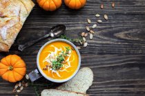 Flat lay of fresh pumpkin soup garnished with sour cream, toasted pumpkin seeds and thyme with homemade artisan bread in the background. — Stock Photo