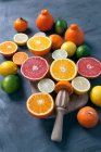 Various halved citrus fruits on a board with a wooden citrus reamer — Stock Photo