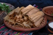 Tamales végétaliens remplis de seitan, masa, chili verde et servis avec sauce ranchero, crème et haricots chili — Photo de stock